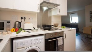 A compact kitchen with a microwave, toaster, stove, and washing machine. - Stayzo Castle Point 18 Apartments - Premier Lodge (Southampton)