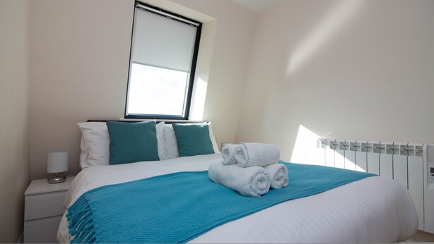 A hotel room with a bed, a window, a nightstand, and a radiator. - Stayzo Premiere Serviced Accommodation - 17 (Southampton)