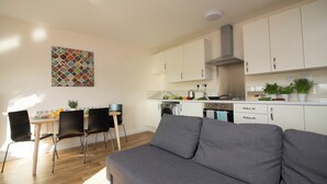 A modern kitchen with white cabinets, a stainless steel range hood, and a dining area with a gray sofa and black chairs. - Stayzo Premiere Serviced Accommodation - 17 (Southampton)