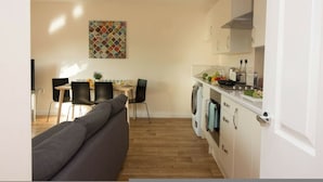 A modern kitchen with white cabinets, a dining area with a gray sofa, and a colorful abstract painting on the wall. - Stayzo Premiere Serviced Accommodation - 17 (Southampton)