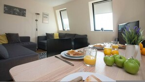 A modern living room with a sofa, a dining table with breakfast items, and a TV. - Stayzo Premiere Serviced Accommodation - 17 (Southampton)
