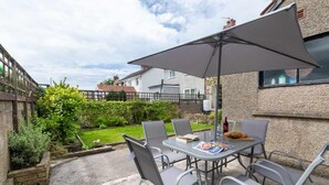 Een terras buiten met een tafel, stoelen, een grote parasol en uitzicht op de tuin.