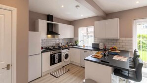 Een moderne keuken met witte kastjes, een zwart aanrecht, een inbouwoven, een wasmachine en een raam met zonwering.