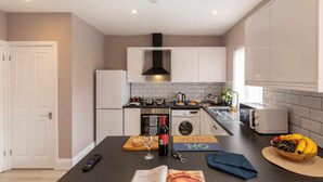 Een moderne keuken met witte kasten, een zwart aanrecht, een centraal eiland met een fles wijn en een schaal fruit.