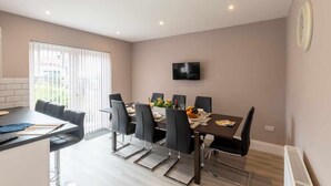 Een moderne eethoek met een lange tafel, zwarte stoelen en een flatscreen televisie aan de muur.