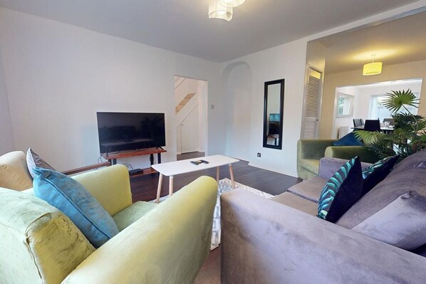 A modern living room with a flat-screen TV, a white coffee table, and two sofas with patterned cushions.