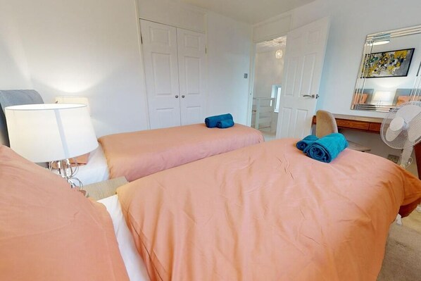 Une chambre d’hôtel avec deux lits, un bureau, une chaise, une lampe et un ventilateur.