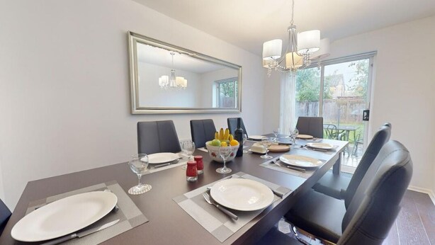 A dining room with a long table set for six, a large mirror above, and a view of the backyard through a sliding glass door. - Parlaunt House - 3 Bedroom With Free Parking (Slough)