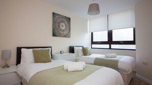 Une chambre d’hôtel avec deux lits, une table de chevet, une lampe, un tableau décoratif et une fenêtre avec des stores.