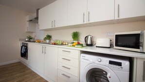 Une cuisine compacte avec des meubles blancs, un lave-linge encastré, un four à micro-ondes et divers ustensiles de cuisine disposés sur le plan de travail.