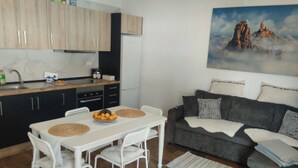 Eine moderne Küche mit Holzausstattung, einem Esstisch mit weißen Stühlen und einem grauen Sofa.