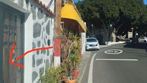 Straßenansicht eines Gebäudes mit steinverkleideter Fassade, einem gelben Markisenvorbau und Blumentöpfen.