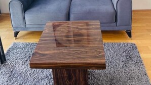 Un canapé gris à motifs, avec une table basse en bois devant, un tapis gris à longues mèches et deux œuvres d’art accrochées au mur au-dessus du canapé.