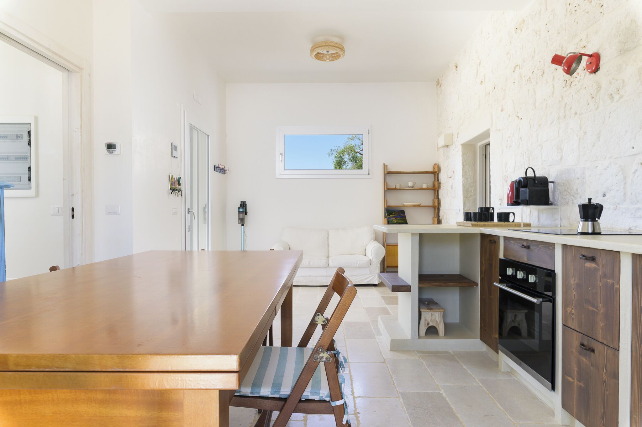 A modern kitchen with a wooden dining table, a white sofa, and a built-in oven.