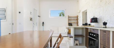 A modern kitchen with a wooden dining table, a white sofa, and a built-in oven.