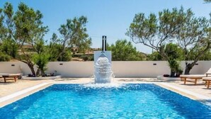 A rectangular swimming pool with clear blue water, surrounded by a low wall and trees. - Fantasy Rooms  (Milos)