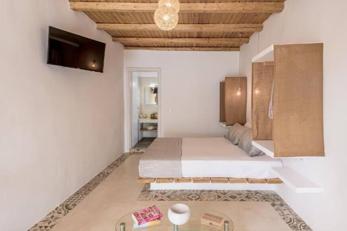 A bedroom with a bed, a TV mounted on the wall, a wooden ceiling, and a patterned floor.