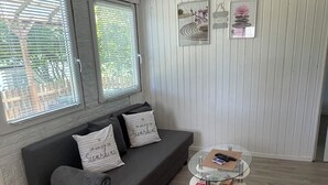 A modern living room with a grey sofa, two pillows, a glass coffee table, and a white wall with framed artwork.