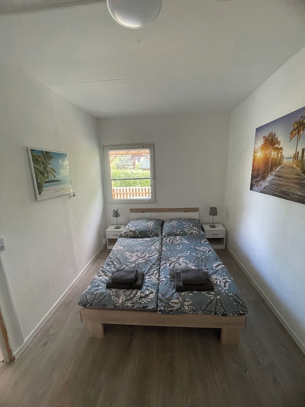 A bedroom with a bed, a window, a nightstand, a lamp, and two wall art pieces.