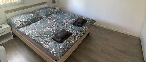 A bedroom with a bed, a nightstand, a lamp, and a painting of a beach scene.