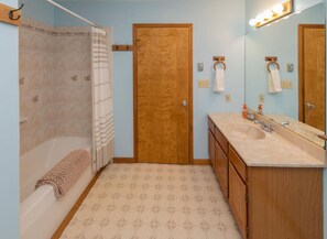 A bathroom with a shower, a sink with a vanity, a wooden door, and a mirror with lights. - Perfect Family Vacation Home in the Mountains (Windham)