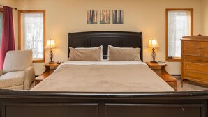 Een netjes ingerichte slaapkamer met een groot bed, twee nachtkastjes met lampen, een fauteuil en een kast.