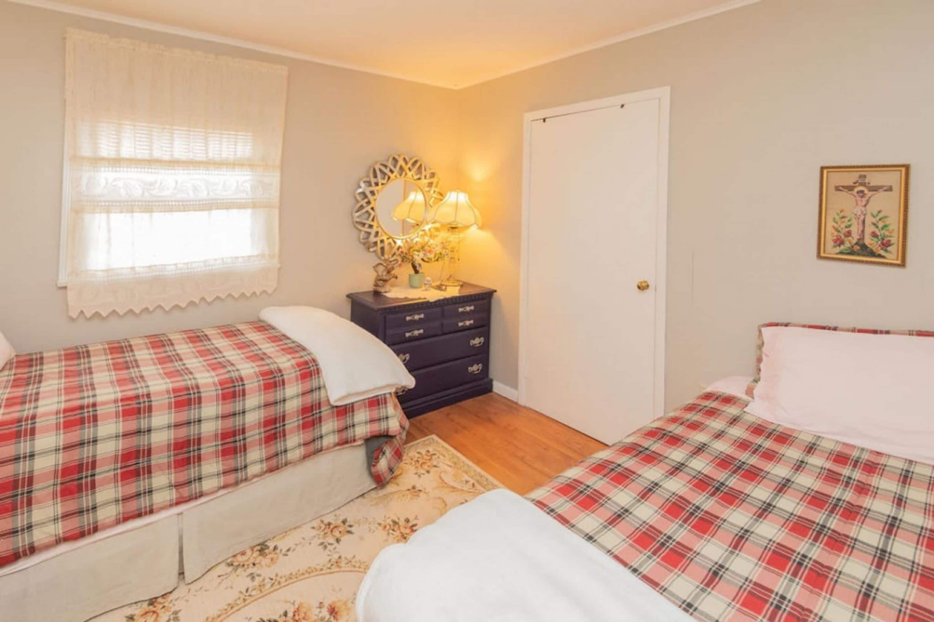 A bedroom with two beds, a dresser, a mirror, a lamp, and a door.