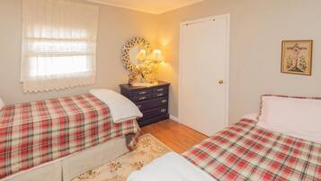 A bedroom with two beds, a dresser, a mirror, a lamp, and a door.