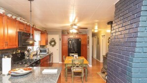 A kitchen with wooden cabinets, a granite countertop, a stove, and a dining area with a table and chairs. - Amazing Hiking Cozy Home Close to Mountns Fireplace (Prattsville)