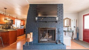A kitchen with a black brick fireplace, wooden cabinets, and a large window. - Amazing Hiking Cozy Home Close to Mountns Fireplace (Prattsville)