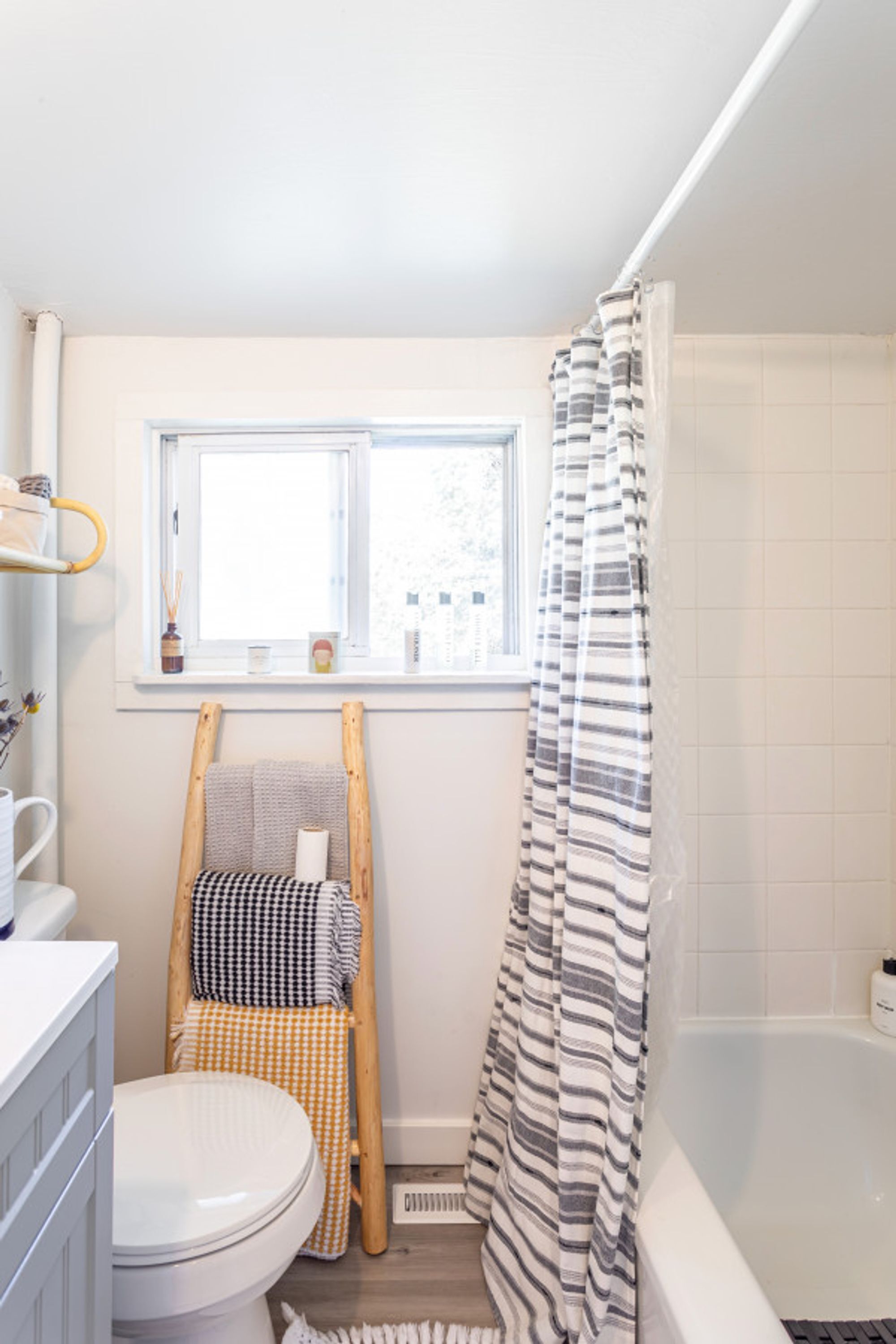 Une petite salle de bain comprenant des toilettes, une fenêtre, une douche avec des rideaux à rayures et une petite chaise en bois.