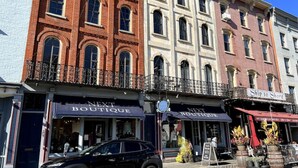 A row of multi-story buildings with storefronts, including a 'Next Boutique' and 'Ship to Shore' restaurant.
