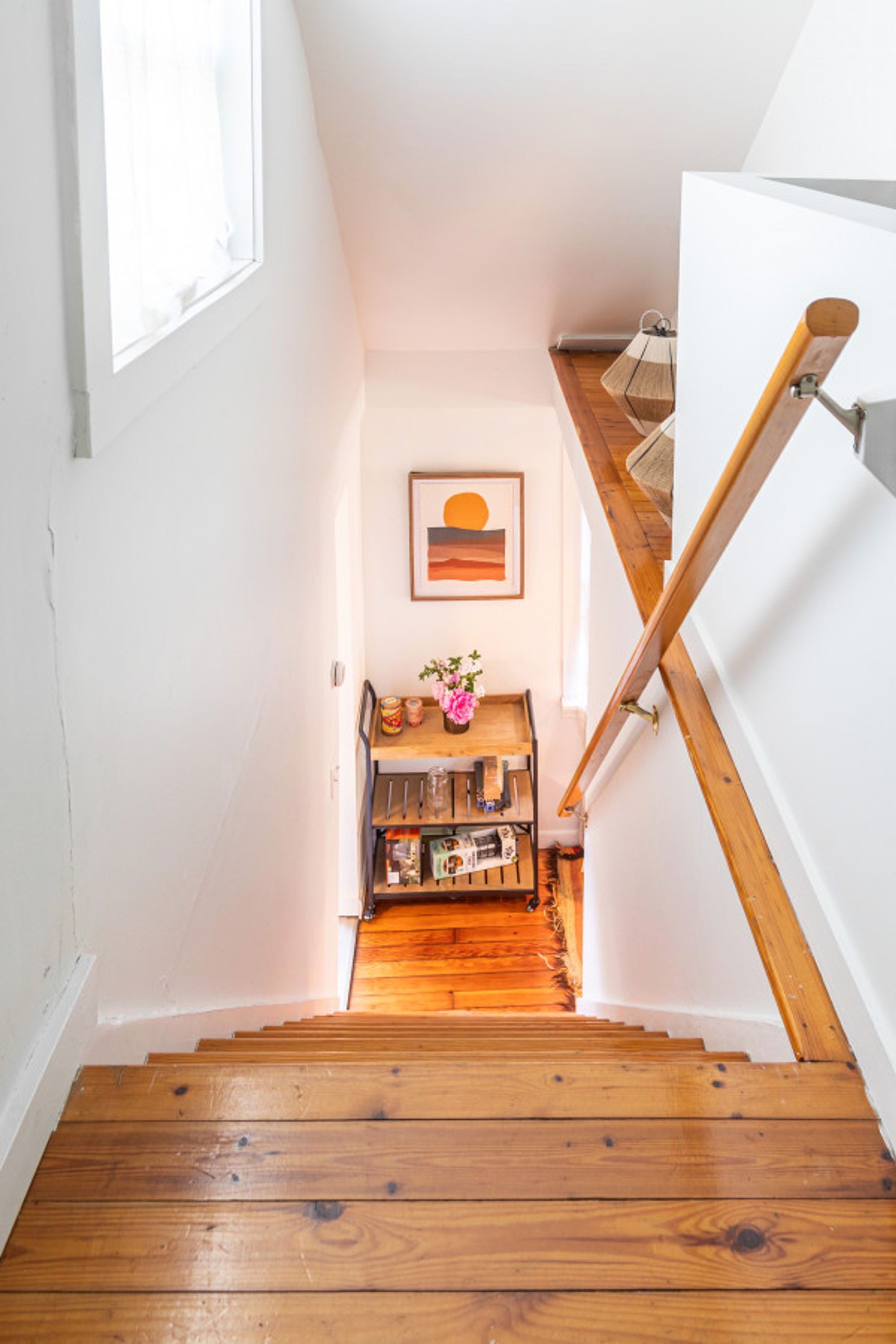 A wooden staircase with a wooden handrail and a small shelf with books and a vase at the bottom.