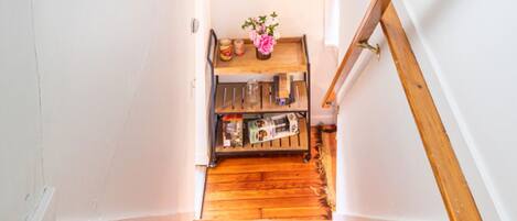 A wooden staircase with a wooden handrail and a small shelf with books and a vase at the bottom.