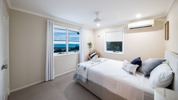 Une chambre avec un grand lit, une fenêtre avec des rideaux, un ventilateur de plafond et un appareil de climatisation.