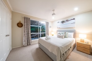 A bedroom with a bed, a nightstand, a window with curtains, and a wall-mounted picture. - Kim's On Kara (Airlie Beach)