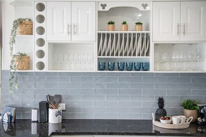 A kitchen with white cabinets, a grey tiled backsplash, and various kitchen items. - Kim's On Kara (Airlie Beach)