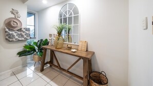 Un couloir avec une console en bois, une grande fenêtre en arc de cercle et des objets décoratifs, notamment un chapeau, des plantes et un panneau d’accueil.