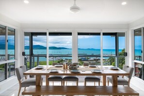 A dining area with a wooden table set for six, large windows offering a view of the sea and marina.