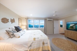 A bedroom with a large bed, a television, a window with a view, and a door.