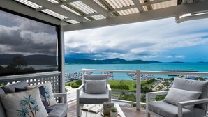 Un balcon avec deux chaises blanches, une table en bois et une vue sur une marina remplie de bateaux.