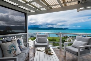 A balcony with two white chairs, a wooden table, and a view of a marina with boats. - Kim's On Kara (Airlie Beach)