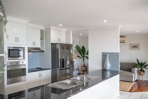 A modern kitchen with white cabinets, stainless steel appliances, and a granite countertop. - Kim's On Kara (Airlie Beach)