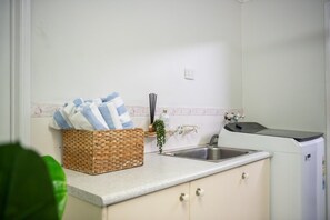 A kitchen with a sink, a washing machine, a basket with towels, and a small plant.