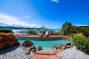 A swimming pool with lounge chairs and a view of the ocean. - Kim's On Kara (Airlie Beach)