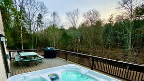 Ein Whirlpool auf einer Holzdielen-Terrasse mit Picknicktisch und Grill, umgeben von Bäumen.