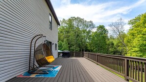 A wooden deck with a hanging chair, a barbecue grill, and a view of a forested area. - Family Fun Oasis Hot Tub Steam Room Pool Stream Firepit Games (Saugerties)