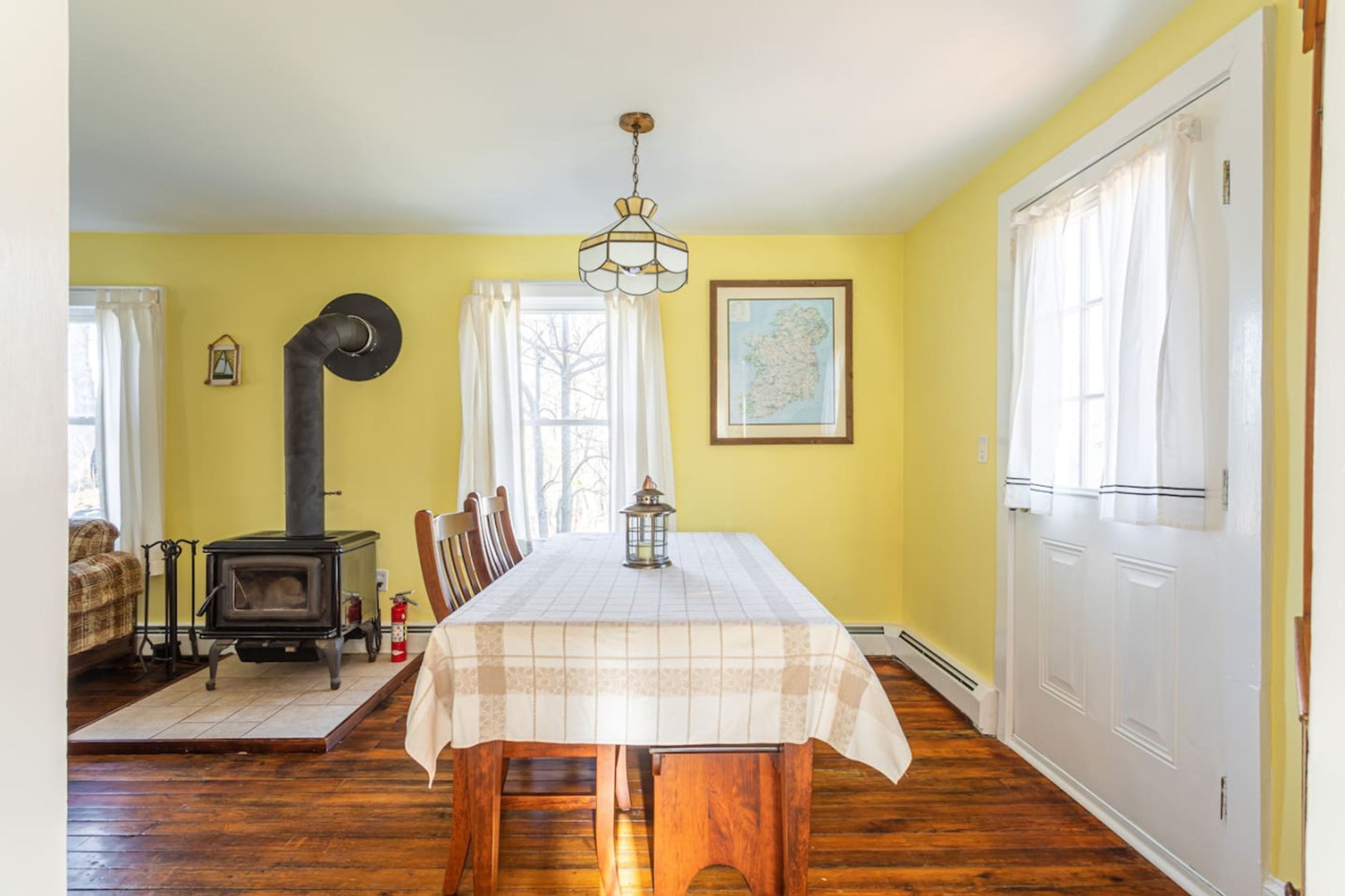 A dining area with a table set for four, a wood-burning stove, and a map on the wall.