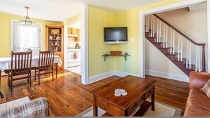 A living room with a wooden coffee table, a television mounted on the wall, and a staircase leading to another level. - Cozy Easy Access to the Best of the Hudson Valley (Cornwall)