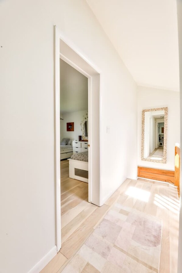 A hallway with a wooden floor leading to a bedroom with a white dresser and a mirror. - Hunter Mountain Ski House - Tesla Charger (Hunter)